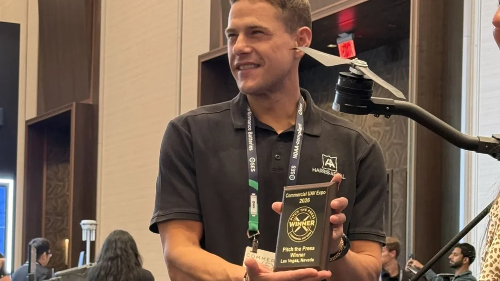 Harris Aerial holding the Commercial UAV Expo 2026 Pitch the Press Winner plaque in Las Vegas, with an H4C Quad arm in frame